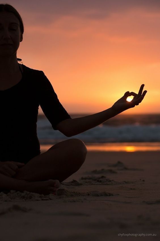 A person meditating on a sandy beach with sunset ocean in background